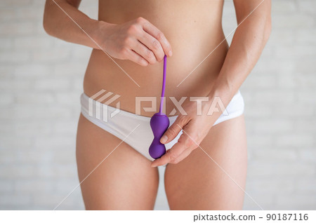 Faceless woman in white panties and with a bare tummy holds a kegel trainer. Latex vaginal vibrator for training the pelvic floor muscles with an antenna. The device for imbuilding. Women Health. 90187116