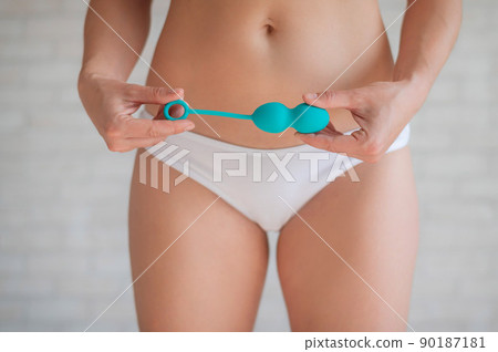 Faceless woman in white panties holding the Kegel trainer for strengthening the intimate muscles of the vagina. Vaginal balls with a displaced center of gravity of a mint color. Sex toy. Faceless woman in white panties holding the Kegel trainer for strengthening the intimate muscles of the vagina. Vaginal balls with a displaced center of gravity of a mint color. Sex toy. 90187181