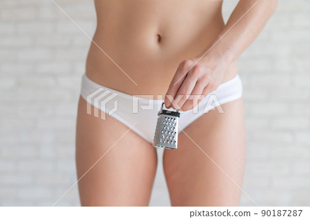 Unrecognizable woman in white panties holds in hands a mini grater. Metaphor of the bristles after depilation in the bikini area of the girl. Spiky hair is an argument for epilation. 90187287