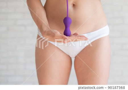 Faceless woman in white panties and with a bare tummy holds a kegel trainer. Latex vaginal vibrator for training the pelvic floor muscles with an antenna. The device for imbuilding. Women Health. 90187368