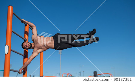 Shirtless man doing human flag outdoors.  90187391