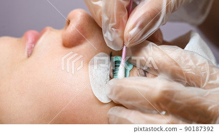 The master removes the composition for lamination from the client's eyelashes with a cotton swab. Eyelash perm procedure. 90187392