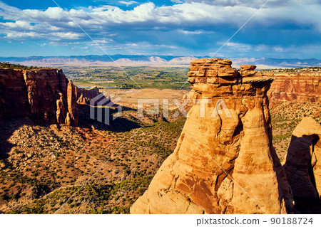 Detail of large red rock pillar in canyon with valley and farms in background 90188724