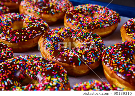 Tray full of fresh baked yeast donuts with chocolate and colorful sprinkles Tray full of fresh baked yeast donuts with chocolate and colorful sprinkles 90189310