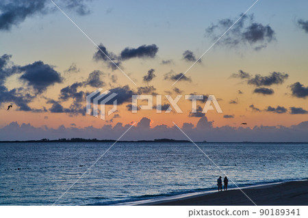 Beach and ocean with two figures during sunset with soft muted sky Beach and ocean with two figures during sunset with soft muted sky 90189341