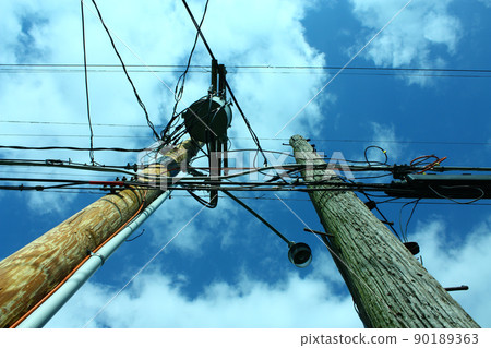 Two telephone poles against a blue but cloudy sky Two telephone poles against a blue but cloudy sky 90189363