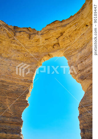 Vertical open natural arch cutting through white stone against blue sky 90189447
