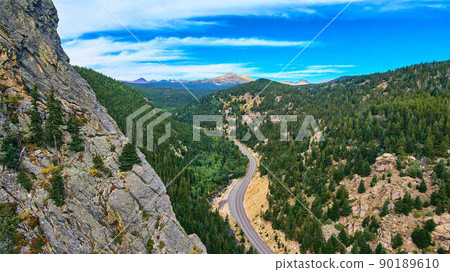 Cliff mountain of rocks next to highway road travelling through pine trees Cliff mountain of rocks next to highway road travelling through pine trees 90189610