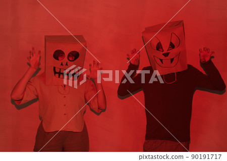 Young people in paper bags with funny grimaces on heads gesturing hands while scaring you in darkness, red light effect 90191717
