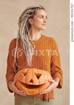 Attractive young craftswoman with dreads holding carved pumpkin and looking away, Halloween concept Attractive young craftswoman with dreads holding carved pumpkin and looking away, Halloween concept 90191787