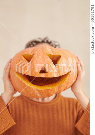 Unrecognizable woman in brown sweater holding funny pumpkin against face while having fun at Halloween party Unrecognizable woman in brown sweater holding funny pumpkin against face while having fun at Halloween party 90191791