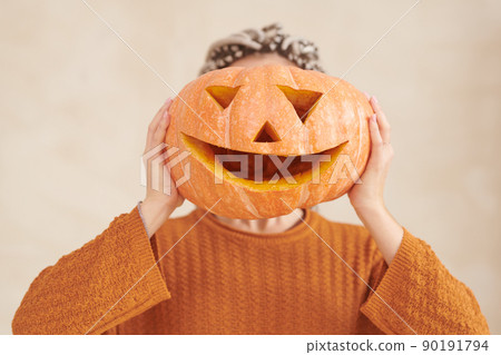 Unrecognizable woman in brown sweater holding funny pumpkin against face Halloween party Unrecognizable woman in brown sweater holding funny pumpkin against face Halloween party 90191794