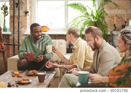 Smiling Afro-American man drinking tea and eating cookies while talking to girl at Halloween party 90191798