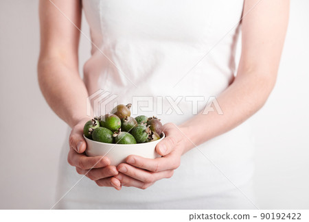 Horizontal medium section shot of unrecognizable woman wearing white clothes holding bowl full of pineapple guava fruits, copy space 90192422