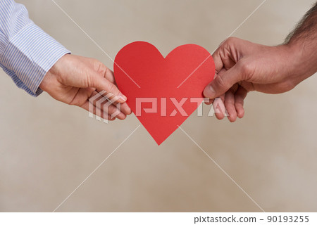 Close-up shot of unrecognizable young man and woman holding red paper heart, St Valentines day concept Close-up shot of unrecognizable young man and woman holding red paper heart, St Valentines day concept 90193255