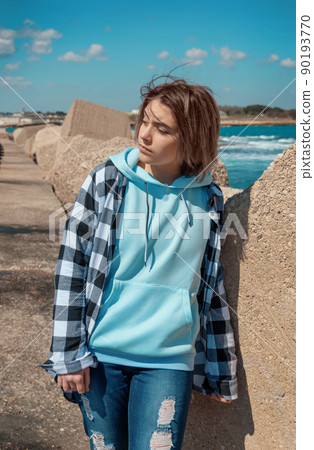 Teenager girl in light blue hoodie and plaid shirt near the sea, Clothing mockup 90193770