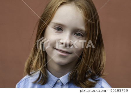Portrait of a red-haired child with green eyes 8 years old in a blue shirt on a teracot background. Portrait of a red-haired child with green eyes 8 years old in a blue shirt on a teracot background. 90195739