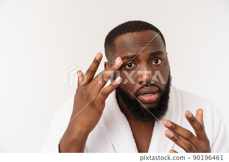 African American man looks at pimples on face. Acne. Male hygiene. Isolated on white background. Studio portrait 90196461