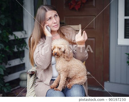 woman sits on terrace with poodle and communicates smartphone. 90197230