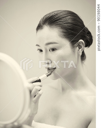 beautiful young asian woman looking in the mirror while applying lipstick on lips, black and white 90198044