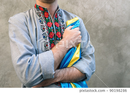 Soft Selective focus Man holds the blue and yellow national flag of Ukraine over his heart. Guy in a traditional embroidered shirt on a background of textured concrete wall. Copy space Soft Selective focus Man holds the blue and yellow national flag of Ukraine over his heart. Guy in a traditional embroidered shirt on a background of textured concrete wall. Copy space 90198286