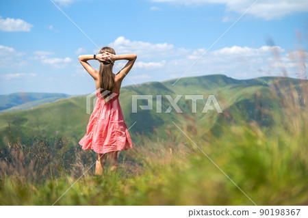 Young woman in red dress standing on grassy field on a windy day in summer mountains enjoying view of nature. Young woman in red dress standing on grassy field on a windy day in summer mountains enjoying view of nature. 90198367
