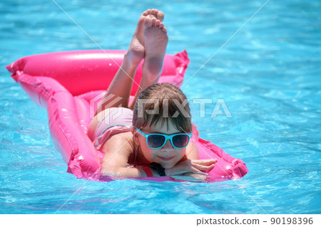 Young child girl relaxing on summer sun swimming on inflatable air mattress in swimming pool during tropical vacations. Summertime activities concept 90198396