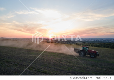 Tractor spraying fertilizers with insecticide herbicide chemicals on agricultural field at sunset 90198593