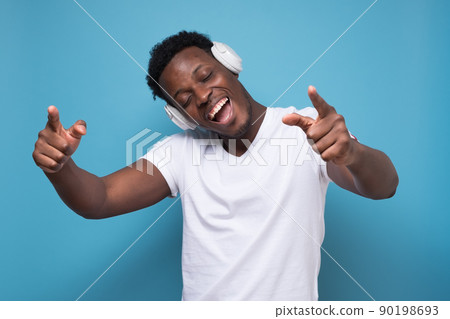 Happy emotive african man listening to music with white earphone. 90198693