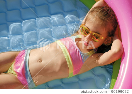 A beautiful girl in a separate colored swimsuit and sunglasses is sunbathing lying in an inflatable swimming pool. Baby sunscreen. Rest in the summer on vacation A beautiful girl in a separate colored swimsuit and sunglasses is sunbathing lying in an inflatable swimming pool. Baby sunscreen. Rest in the summer on vacation 90199022