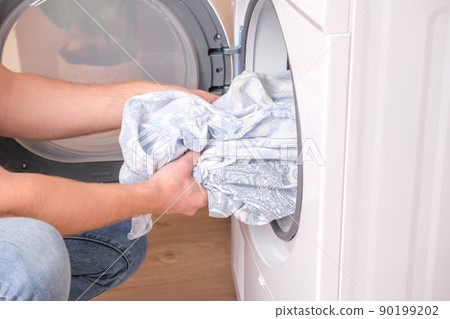 A man takes dried bed linen out of the dryer A man takes dried bed linen out of the dryer 90199202