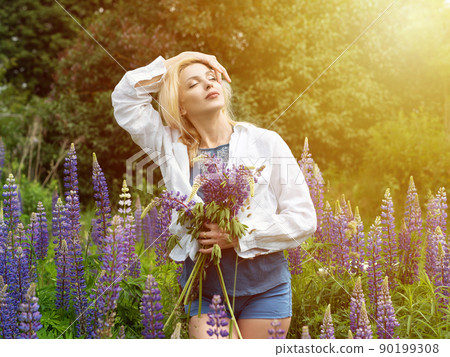 Woman walks in the garden full of lupines Woman walks in the garden full of lupines 90199308