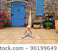 happy baby sits on porch front facade beautiful brick, Italian, Spanish house. Rustic terrace. large wooden blue door and shutters on window. child plays summer yard. 90199649