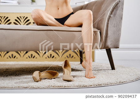 Barefoot legs of woman on the couch next to shoes 90209437