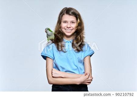 Child girl with pet green quaker parrot looking at camera on light studio background 90210792