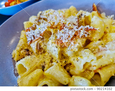 Penne pasta carbonara on white sauce with bacon and extra topping cheese served on blue plate 90214102