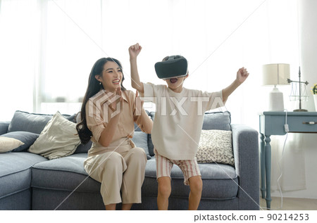Smiling mother looking son playing games using virtual reality headset(VR) at home. Technology future concept. 90214253