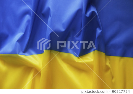 Close up shot of ruffled Ukrainian yellow and blue flag with a lot of copy space for text. Textured background. 90217734