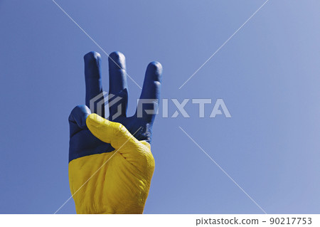Man's hand lit by sunshine painted in colors of Ukrainian national flag showing a traditional trident hand gesture as a symbol of support and solidarity with Ukraine. Copy space, close up, background. Man's hand lit by sunshine painted in colors of Ukrainian national flag showing a traditional trident hand gesture as a symbol of support and solidarity with Ukraine. Copy space, close up, background. 90217753