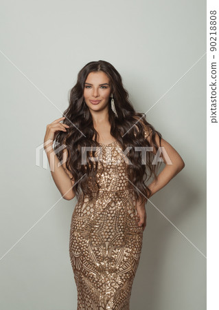 Happy smiling cheerful woman with long dark wavy hairstyle in gold dress standing  90218808