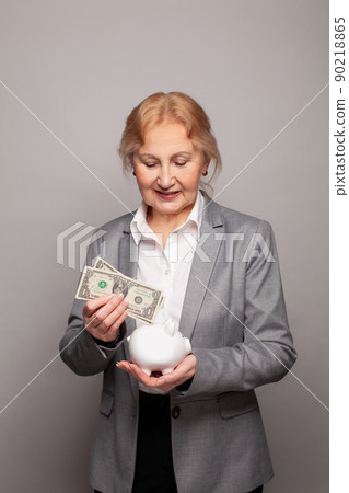 Portrait of woman 60 s years old holding US dollars and piggy bank 90218865
