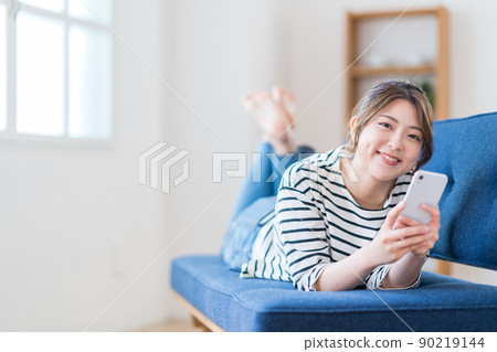 A young woman operating a smartphone with a sofa A young woman operating a smartphone with a sofa 90219144