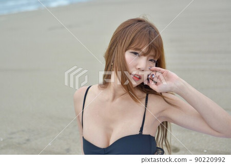 A young woman in a black bikini posing on a sandy beach A young woman in a black bikini posing on a sandy beach 90220992