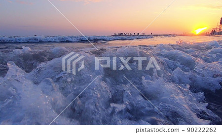 Very low angle shot of sea waves crashing on sandy beach. People walking. Sandy beach, sea coast, sunset dawn sunset sunrise. Sunny path. Seascape, waterscape background. Slow motion. Sea wave inside 90222262