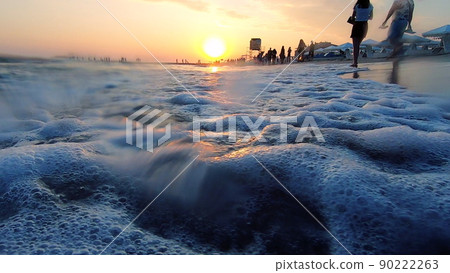 Very low angle shot of sea waves crashing on sandy beach. People walking. Sandy beach, sea coast, sunset dawn sunset sunrise. Sunny path. Seascape, waterscape background. Slow motion. Sea wave inside 90222263