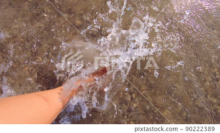 Girl with bare feet walking on water on sandy beach of sea and splashes water her feet on summer sunny day. Barefoot on sand beach. Vacation enjoyment rest relax travel tourism holiday. Slow motion 90222389
