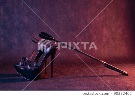 Black shiny high heel shoes and a whip on a dark background 90222403