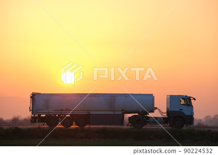 Semi-truck with tipping cargo trailer transporting sand from quarry driving on highway hauling goods in evening. Delivery transportation and logistics concept 90224532