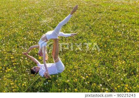 Beautiful young couple doing acro yoga in park. Man lying on grass and balancing woman in his feet. Beautiful young couple doing acro yoga in park. Man lying on grass and balancing woman in his feet. 90225243