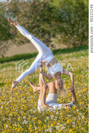Beautiful young couple doing acro yoga in park. Man lying on grass and balancing woman in his feet. Beautiful young couple doing acro yoga in park. Man lying on grass and balancing woman in his feet. 90225248
